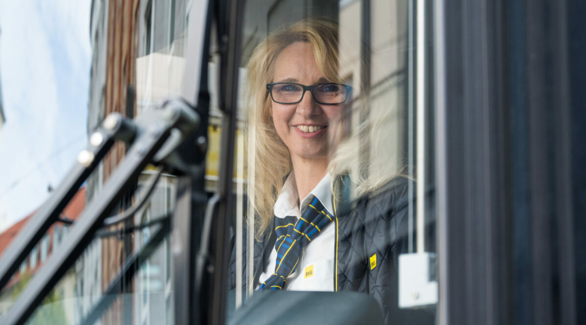 Anett ist Straßenbahnfahrerin bei der BVG. Sie sitzt lächelnd hinter dem Steuer einer Tram.
