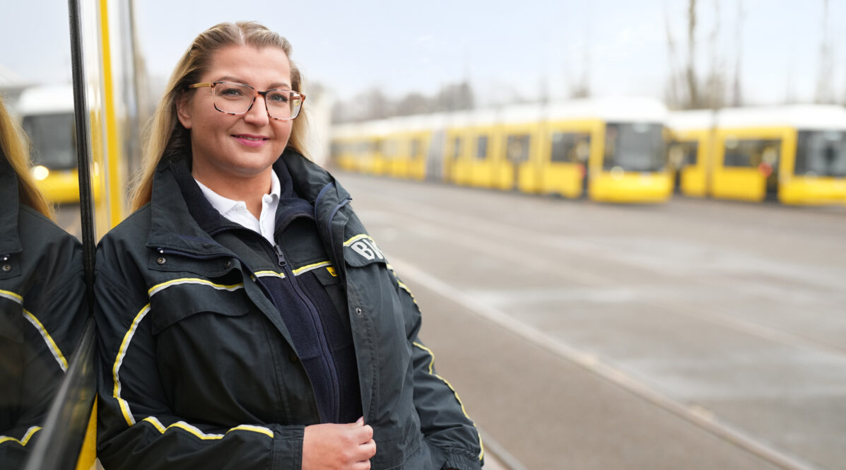 Frau in BVG-Fahrdienstkleidung steht vor Straßenbahnen auf einem Betriebshof