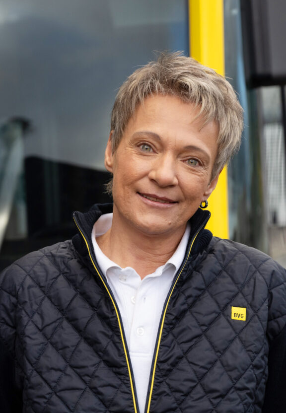 Portraitfoto: Simone steht in BVG-Dienstkleidung für Fahrerinnen vor einem BVG Bus