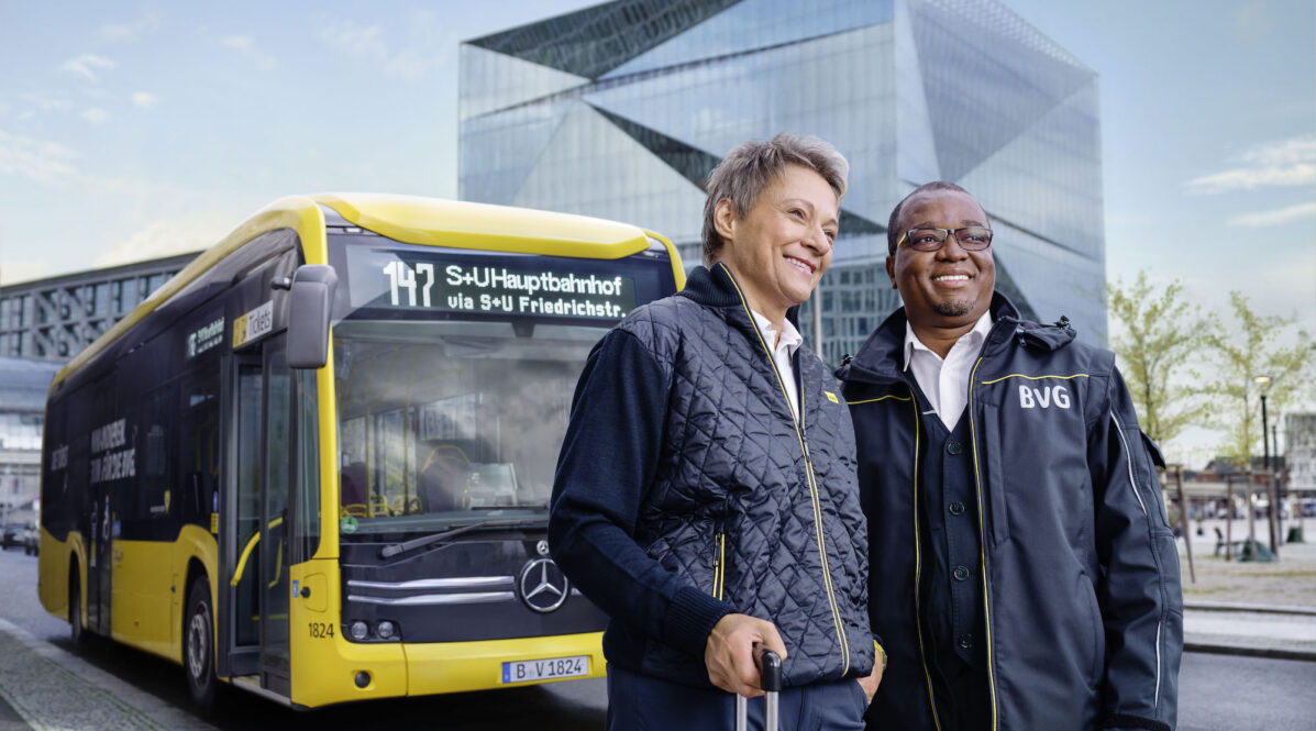 Eine Frau und ein Mann in BVG-Fahrdienstkleidung stehen vor einem BVG-Bus in Berlin Mitte vor dem Gebäude Cube