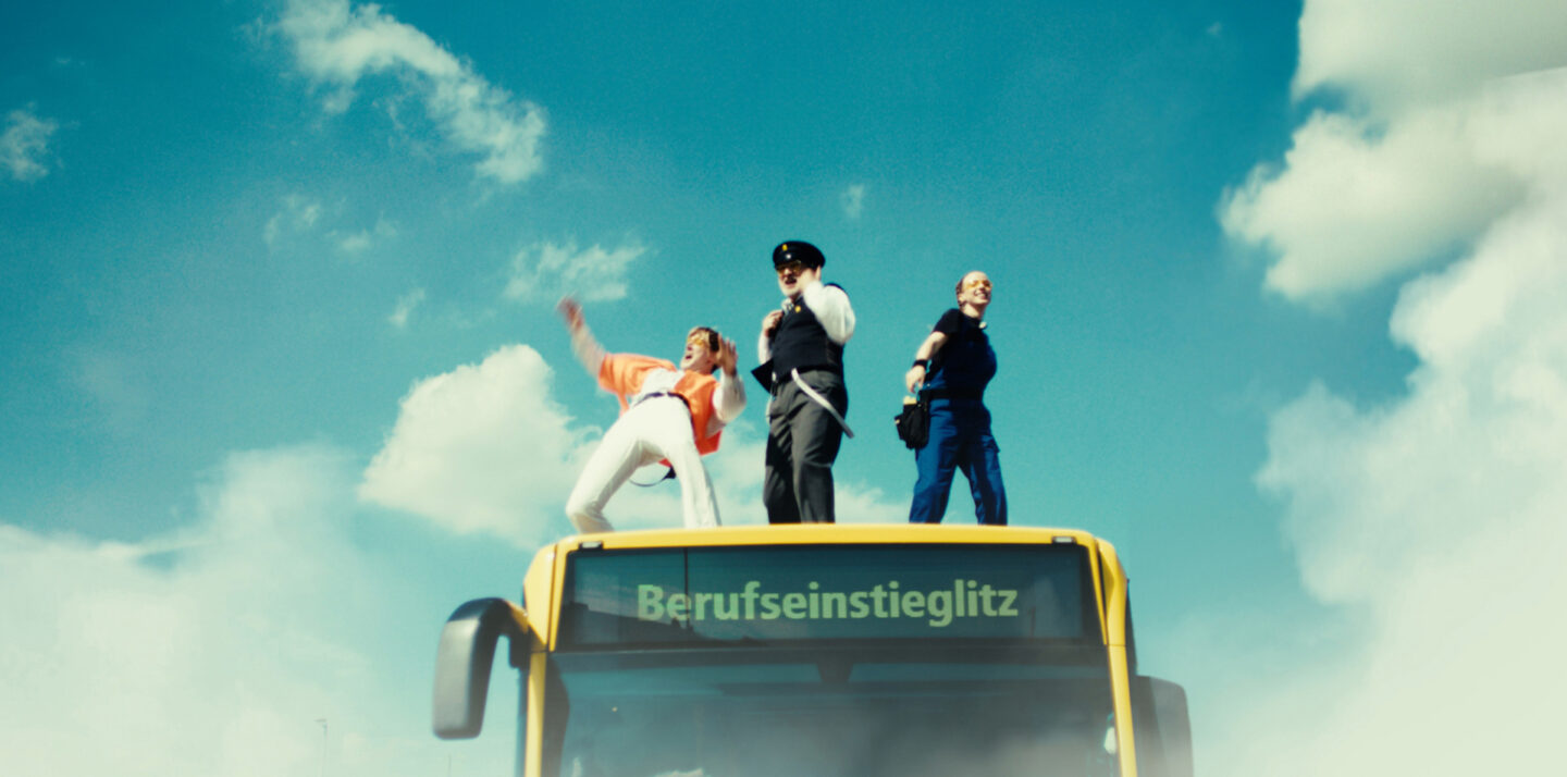 Screenshot aus Arbeitgeber-Clip. Drei Personen, die auf einem Bus tanzen.