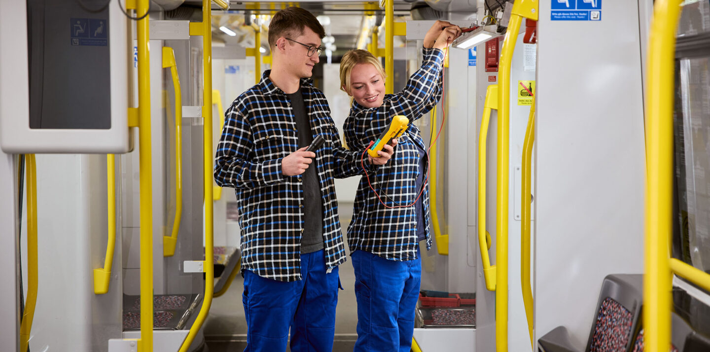 Zwei Elektroniker für Betriebstechnik prüfen etwas in der U-Bahn