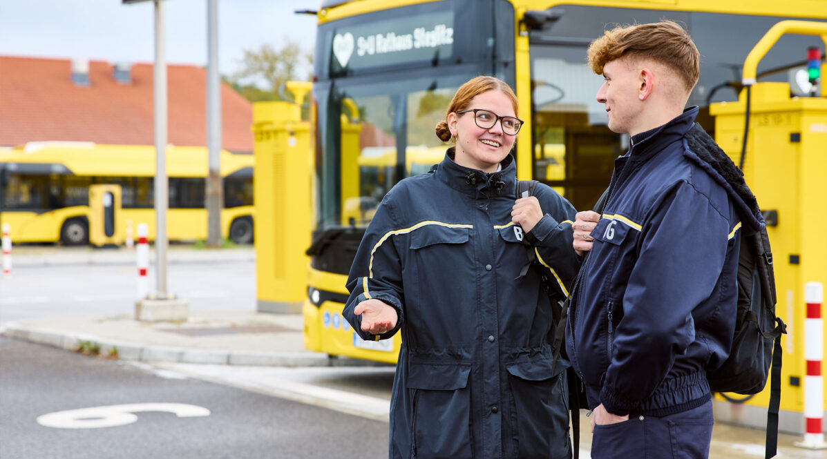 Zwei Personen aus dem Fahrdienst unterhalten sich, im Hintergrund sieht man einen E-Bus.